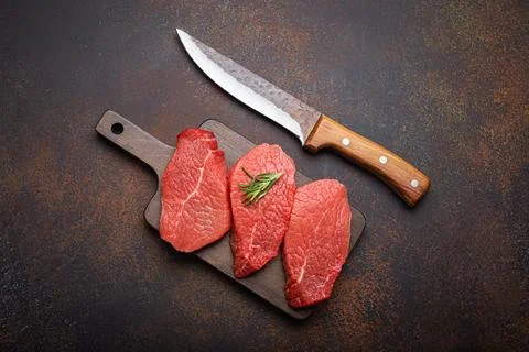 Three raw uncooked meat beef top sirloin steaks on wooden cutting board with Foto stock