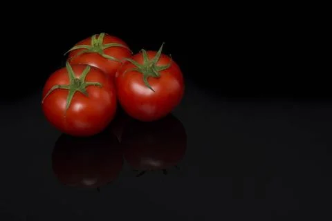 Three real tomatoes in a triangle on a black background with reflection Th... Stock Photos