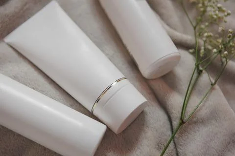 Three rectangular white lotion tubes on linens next to a flower Stock Photos