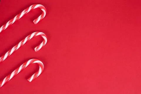Three red and white candy canes on red christmas background, top view with copy Stock Photos