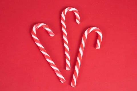 Three red and white candy canes on red christmas background, top view, mock up Stock Photos
