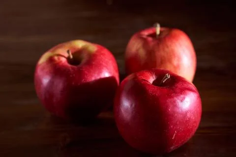 Three red apples lie on a cinnamon wooden table Stock Photos