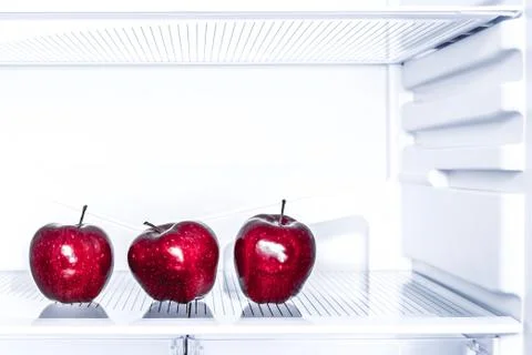 Three red apples is lying on the empty shelf of the fridge. Diet concept Stock Photos
