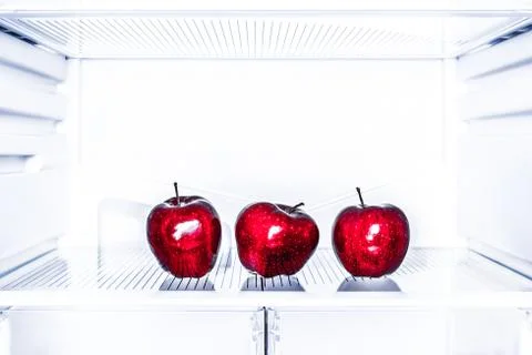 Three red apples is lying on the empty shelf of the fridge. Toned. Diet concept Stock Photos