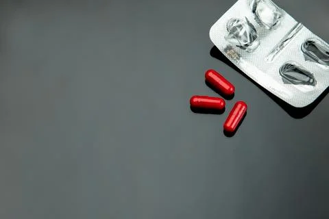 Three red capsules for treatment with an empty package on a dark background Stock Photos