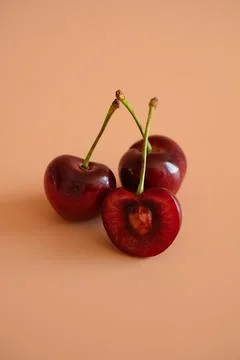 Three red cherries on peach background Stock Photos