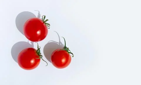 Three red cherry tomatoes with green stalks and tough shadow on a white Stock Photos