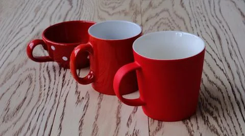 Three red cups of different shapes standing diagonally in a row on a wooden b Stock Photos
