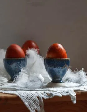 Three red easter eggs in blue egg stands on white feathers on a linen napkin Stock Photos