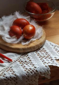 Three red easter eggs on white feathers on a linen napkin, close-up Stock Photos