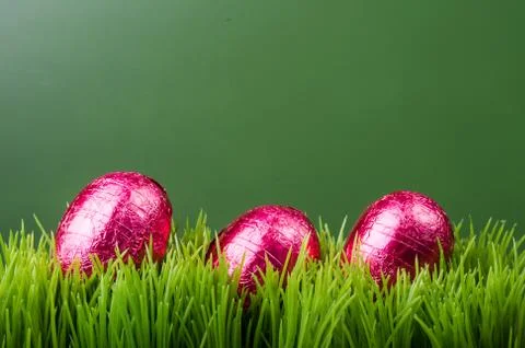 Three red foil easter eggs on grass 스톡 사진
