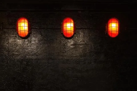Three red glowing nautical lights on dark textured wall Stock Photos