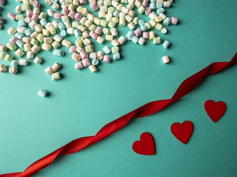 Three red hearts and multicolored candies, and between them lies a red ribbon Stock Photos