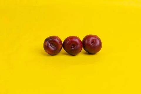Three red plums on yellow background Stock Photos
