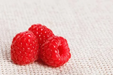 Three red ripe raspberry fruit, on gray linen table cloth, macro Foto stock