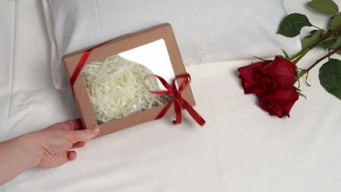 Three red roses and a box with a gift on white bed linen. Holiday concept. Stock Footage 169599219