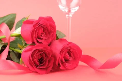 Three red roses on a red background with a ribbon and a glass Stock Photos