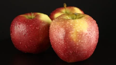 Three red ruddy apples with water droplets rotates on a black background. Video stock 151520176