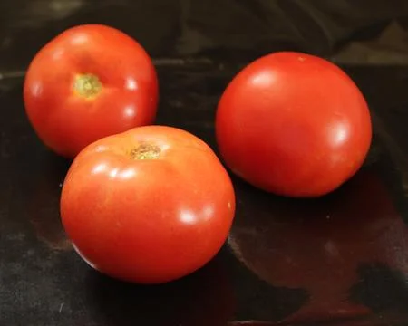 Three red tomatoes on a black background Stock Photos