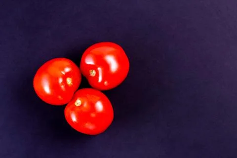 Three red tomatoes on a dark texture surface with space to copy Stock Photos