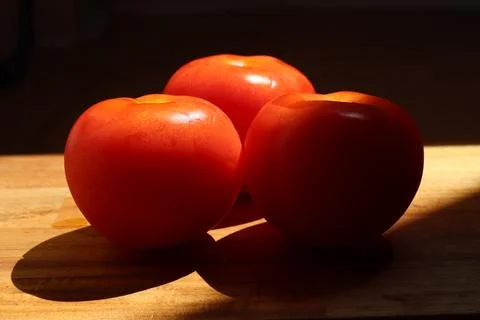 Three red tomatoes in sunlight on kitchen cutting board Stock Photos