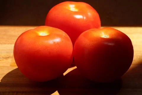 Three red tomatoes in sunlight on kitchen cutting board Stock Photos