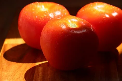 Three red tomatoes in sunlight on kitchen cutting board Stock Photos