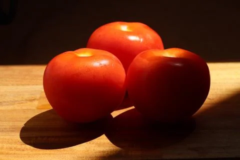 Three red tomatoes in sunlight on kitchen cutting board Stock Photos