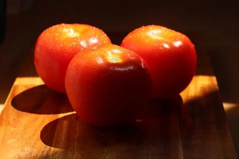 Three red tomatoes in sunlight on kitchen cutting board Stock Photos