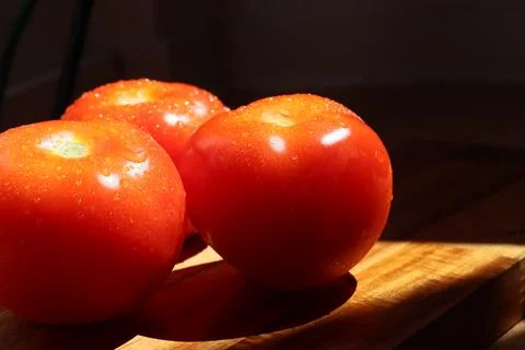 Three red tomatoes in sunlight on kitchen cutting board Stock Photos