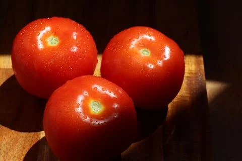 Three red tomatoes in sunlight on kitchen cutting board Stock Photos