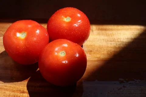 Three red tomatoes in sunlight on kitchen cutting board Stock Photos