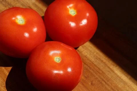 Three red tomatoes in sunlight on kitchen cutting board Stock Photos