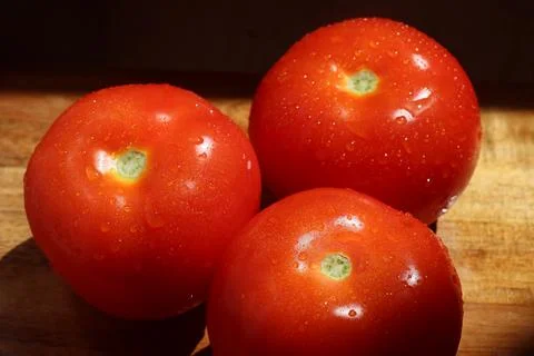 Three red tomatoes in sunlight on kitchen cutting board Stock Photos