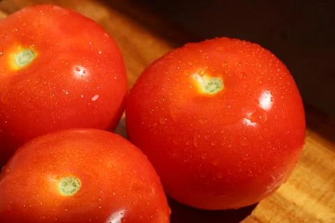 Three red tomatoes in sunlight on kitchen cutting board Stock Photos