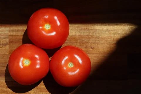 Three red tomatoes in sunlight on kitchen cutting board Stock Photos