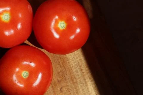 Three red tomatoes in sunlight on kitchen cutting board Stock Photos
