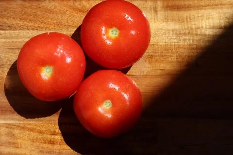 Three red tomatoes in sunlight on kitchen cutting board Stock Photos