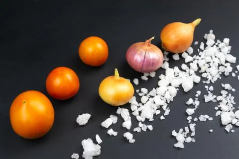 Three red tomatoes, three onions and coarse salt on a black background. Stock-Fotos