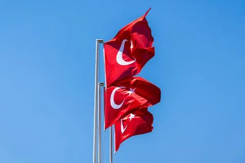 Three red Turkish flags bearing white crescent and star wave on poles Stock Photos