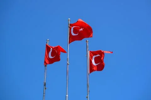 Three red Turkish flags flutter on flagpole against bright blue sky, with Stock Photos
