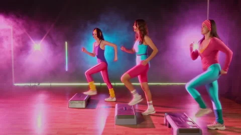 Three Retro Girls Exercising at Step Aerobics Class in Neon Light and Smoke Stock Footage 328370288