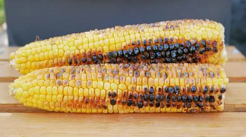 Three ripe fried corn lie next to the barbecue in nature Stock-Fotos