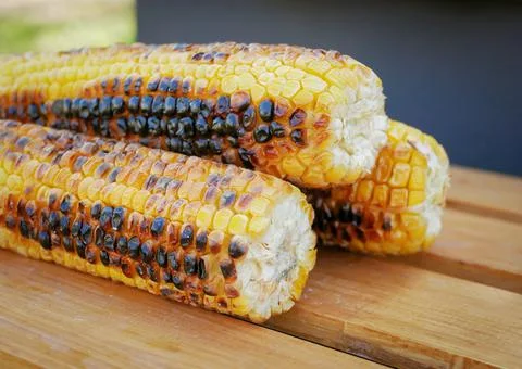 Three ripe fried corn lie next to the barbecue in nature Stock-Fotos