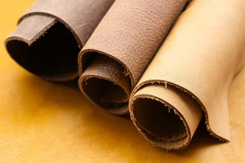 Three Rolled Leather Hides in Dark Brown and Natural Tan Tones on Yellow Ba.. Stock Photos