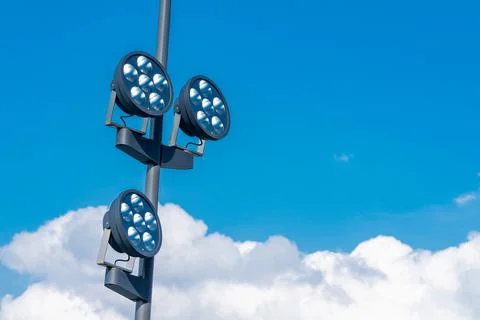 Three round bright floodlights mounted on a pole under a blue sky Stock Photos