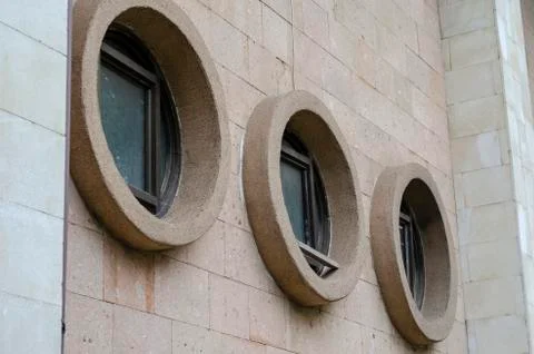 Three round windows with square window frames inside on facade of stone wall. Stock Photos