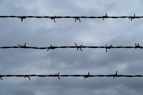 Three rows of barbed wire in front of the dark and cloudy sky - security conc Stock Photos