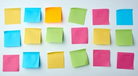 Three rows of blank square paper multicolored stickers on a white wall Stock Photos