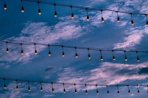 Three rows of warm white light bulbs turn on with the sky in the background. Stock Photos